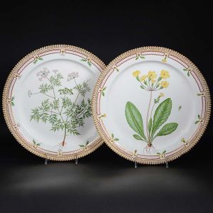 <b>Par de travessas circulares</b> em porcelana dinamarquesa da importante manufatura Royal Copenhagen, modelo <b>"Flora Danica"</b>. Cada peça, inteiramente pintada à mão em belíssima policromia com suas designações botânicas e numeração no verso. Apresenta borda em mínimos picotados cobertos a folha de ouro. Diâm. 36 cm