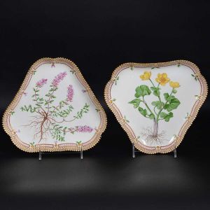<b>Par de covilhetes</b> triangulares em porcelana dinamarquesa da importante manufatura Royal Copenhagen, modelo <b>"Flora Danica"</b>. Cada peça, inteiramente pintada à mão em belíssima policromia com suas designações botânicas e numeração no verso. Apresenta borda em mínimos picotados cobertos a folha de ouro. Compr. 21 cm