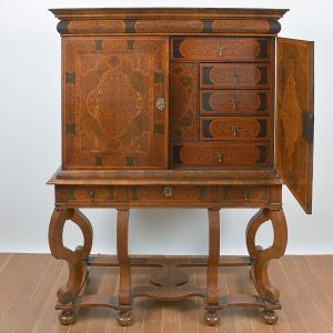 <b>Móvel inglês</b> georgiano, conhecido como "cabinet on stand", construído em diversos cortes de nogueira com belíssimos arabescos fitomorfos. Parte superior com duas portas rebatíveis e gavetas de vários tamanhos centralizando cofre com segredo em seu fundo. Base com gavetão e pernas em curva e contracurva unidas por travessões inferiores. Pés em bolachas. Séc. XVIII. Med. 176 x 126 x 52 cm
