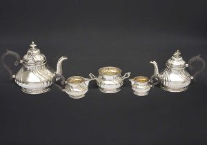 <B>Serviço para chá e café </b>em prata austro-húngara com peças bojudas decoradas com gomos torcidos em estilo neorrococó. Alças em madeira recamadas por volutas e pegas das tampas em pinos. Séc. XIX ou início do séc. XX (1866/1922). Constando de bule para café, bule para chá, leiteira, açucareiro e cremeira. Alt. do bule de café 19 cm. Peso 2030 gramas.