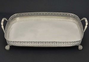 Belo <b>tabuleiro</b> retangular de cantos arredondados em prata portuguesa. Fundo liso. Galeria vazada com geometrizados e recortes. Alças modeladas em delfins e robustos pés em garras. Contraste da cidade de Lisboa do início do séc. XIX. Prateiro JOÃO RAMOS ORTIZ registrado em 1810. Med. 50,5 x 34,5 cm. Peso 2540 gramas.