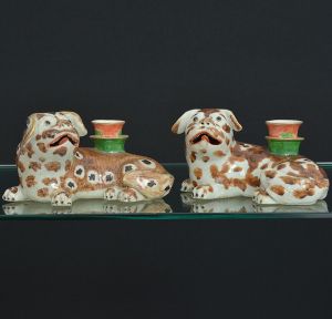 <b>Par de castiçais em forma de cães de fó</b> ("foo dogs"), em porcelana Companhia das Índias policromada, em tonalidades de castanho sobre fundo branco, com receptáculos na cor verde e "rouge de fer" e frisos a ouro. Circa 1830. Pequeno reparo na borda e base de um dos castiçais. Compr. 17 cm; Alt. 9 cm
