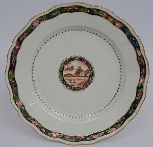<b>Marquês de Bonfim </b>(José Francisco de Mesquita) - <b>Prato raso</b> circular em porcelana Companhia das Índias pertencente ao serviço de jantar do referido nobre. Ao centro reserva em sépia com paisagem lacustre e faixas floridas em policromia sobre fundo negro filetado a ouro. Séc. XIX. Referências bibliográficas à pág. 114 do livro "Louça da Aristocracia no Brasil", por Jenny Dreyfus. Diâm. 23,5 cm