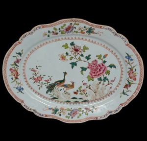 <b>Travessa</b> oblonga em porcelana Companhia das Índias decorada em policromia nos esmaltes da Família Rosa pertencente ao Serviço Real de D. João VI, conhecido como "Serviço dos Pavões". Centro decorado com dois pavões sobre rochedo cercado de peônias. Borda em ondulações com quatro composições floridas. Séc. XVIII. Referências bibliográficas nos mais renomados livros de porcelana já editados. Med. 35 x 27 cm