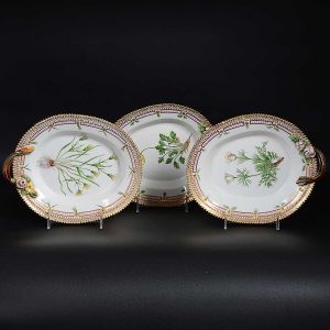 <b>Conjunto de 3 travessas ovais com alça </b>em porcelana dinamarquesa da importante manufatura Royal Copenhagen, modelo <b>"Flora Danica"</b>. Cada peça, inteiramente pintada à mão em belíssima policromia com suas designações botânicas e numeração no verso. Apresenta borda em mínimos picotados cobertos a folha de ouro. Med. 25 x 20 cm