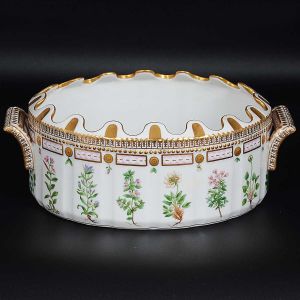 Excepcional <b>"rafraîchissoir" oval</b> de borda ondulada em porcelana dinamarquesa da importante manufatura Royal Copenhagen, modelo <b>"Flora Danica"</b>. Inteiramente pintada à mão em belíssima policromia com suas designações botânicas e numeração no verso. Apresenta borda em mínimos picotados cobertos a folha de ouro. Med. 33 x 23 cm