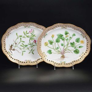<b>Par de travessas ovais</b> com bordas reticuladas em porcelana dinamarquesa da importante manufatura Royal Copenhagen, modelo <b>"Flora Danica"</b>. Cada peça, inteiramente pintada à mão em belíssima policromia com suas designações botânicas e numeração no verso. Apresenta borda em mínimos picotados cobertos a folha de ouro. Med. 27 x 22,5 cm