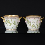 <b>Par de "cachepots" com alças</b>, em porcelana dinamarquesa "Royal Copenhagen", modelo <b>"Flora Danica"</b>, profusamente decorados em policromia com ramagens e botões de flores em relevo e bordas douradas. Cada qual com sua identificação botânica no verso. Alt. 16,5 cm; Diâm. 25,5 cm