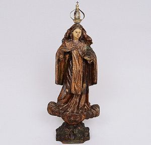 Imagem de <b>Nossa Senhora</b> esculpida em madeira, apresentando policromia e resquícios de ouro com vestes drapeadas em sentido longitudinal. Base em enrolados de nuvens, olhos em contas e coroa de prata. Séc. XVIII. Falta uma mão. Alt. sem a coroa 39 cm
