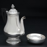 <b>MAISON CHRISTOFLE</b> - Lote constando de: a) Conjunto de 9 lavandas em metal espessurado a prata, sendo 8, modelo "croisé" e 1 com frisos. Diâm. 12 cm; b) Bule para café modelo "Malmaison" com alça em madeira ebanizada. Ambas as peças com marca da "orfèvrerie" nas bases. Alt. 24,5 cm