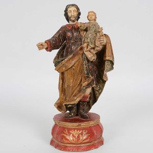 Imagem de <b>São José de botas com Menino Jesus</b> em madeira com faces, mãos e pés em marfim. Rica policromia florida com vestes entalhadas e coturnos negros. Realces a ouro. Base vermelha com delicada composição vegetal à frente. Séc. XVIII. Alt. 26,5 cm