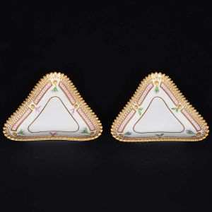 <b>Par de saleiros</b> triângulares em porcelana dinamarquesa da importante manufatura Royal Copenhagen, modelo <b>"Flora Danica"</b>. Cada peça inteiramente pintada à mão em belíssima policromia com suas designações botânicas e numeração no verso. Apresenta borda em mínimos picotados cobertos a folha de ouro. Med. 12 x 10 cm