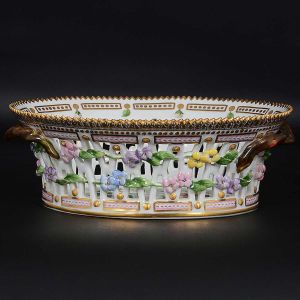 <b>Fruteira oval </b>em porcelana dinamarquesa da importante manufatura Royal Copenhagen, modelo <b>"Flora Danica"</b>. Peça inteiramente pintada à mão em belíssima policromia com suas designações botânicas e numeração no verso. Apresenta borda em mínimos picotados cobertos a folha de ouro. Med. 23 x 18,5 cm