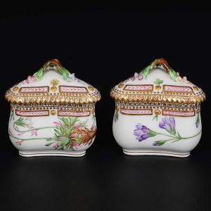 <B>Par de cremeiras</B>, em porcelana dinamarquesa da importante manufatura Royal Copenhagen, modelo "Flora Danica". Cada peça inteiramente pintada à mão em belíssima policromia com suas designações botânicas e numeração no verso. Apresenta borda em mínimos picotados cobertos a folha de ouro. Alt. 8 cm