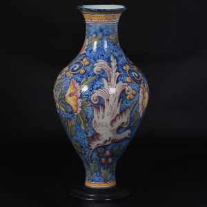 Grande <b>vaso</b> balonado em cerâmica portuguesa Alcobaça decorada com pássaros, flores e arabescos vegetais em ricas composições policromadas, predominando tonalidades de azul e amarelo. Base circular em madeira. Restaurado no gargalo. Alt. 58 cm