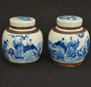 Antigo <b>par de potiches</b> bojudos em porcelana chinesa "craquelê" decorada em azul índigo com figuras de sábios em cena de exterior. Uma tampa com imperceptível bicadinho. Alt. 14,5 cm