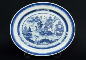 Grande <b>travessa oval</b> em porcelana Companhia das Índias decorada em azul índigo "underglaze". Apresenta paisagem lacustre com personagens, embarcações e pagodes sobre fundo branco. Abas interna e externa em arabescos. Início do séc. XIX. Med. 54 x 45 cm