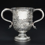 <b>Taça</b> em prata inglesa do período George III. Apresenta bojo decorado com relevo de flores e reserva em uma das faces. Duplas alças recurvadas. Contraste da cidade de Londres de 1767 e marca do prateiro THOMAS WALLIS. Alt. 15 cm; Compr. sem as alças 19,5 cm. Peso 395 gramas.