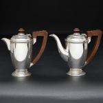 <b>Conjunto de bule de café e leiteira</b>, em prata inglesa, de bojos lisos com delicados filetados com lacinhos na borda. Tampos em degraus. Alça e pegas em madeira. Contraste da cidade de Birmingham de 1937 e marcas de prateiro. Alt. 15,5 cm. Peso 495 gramas.