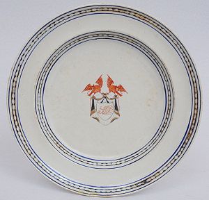 <b>Prato</b> circular em porcelana Companhia das Índias tendo ao centro o monograma de Manoel José Clemente Pinto inserido em reserva encimada por duas aves. Caldeira e borda com frisos azuis. Séc. XIX. Circa 1815. Diâm. 20 cm