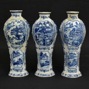 <b>"Garniture" </b>composta de três vasos em forma de bulbos alongados, em porcelana Companhia das Índias, decorados em azul índigo "underglaze" com paisagens lacustres com personagens e pagodes inseridos em reservas superpostas. Restante dos bojos texturizados. Dois deles com restauro, sendo um no bocal e outro na lateral superior. Séc. XVIII. Alt. 29 cm