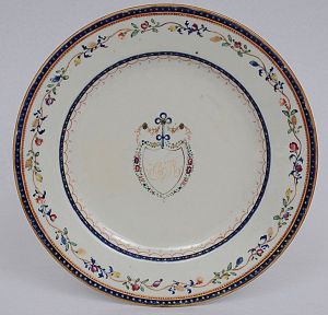 <b>Prato</b> circular em porcelana Companhia das Índias, apresentando ao centro reserva monogramada circundada por flores. Borda também com flores e folhagens e filete com estrelinhas a ouro sobre fundo azul. Período Jiaqing. Diâm. 19,5 cm