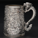 <b>"Mug" </b>em prata profusamente decorada com diversos personagens e figuras de animais tendo ao fundo casario. Pequena reserva oval monogramada com alça modelada em figura de animal bizarro. Contraste no verso. Alt. 10,5 cm. Peso 350 gramas.