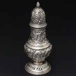 <b>Polvilhador</b> em prata inglesa, em feitio de torre, profusamente decorado com flores e volutas. Contraste da cidade de Chester de 1912 e marca de prateiro. Alt. 15 cm. Peso 90 gramas.