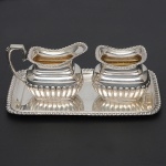 <b>Conjunto de pequena bandeja, leiteira e açucareiro</b> em prata alemã 800 ml com decoração em godrões. Med. da bandeja 17,5 x 10,5 cm; Alt. da leiteira 6,5 cm. Peso 185 gramas.
