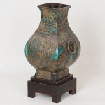 Belíssimo <b>vaso arcaico</b> em bronze chinês lavrado e policromado com parte inferior bojuda e gargalo quadrangular levemente aberto. Pegas laterais com argolas. Pertenceu à importante coleção Regina Ferraz. Datado provavelmente da dinastia Han porém sem garantias. Acompanha base em madeira. Fundo com orifício central já tendo sido usado como abajur. Alt. 36 cm. Larg. 20 cm