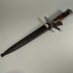 MILITARIA (10) - ADAGA de Oficial do Exército Suíço - Bainha metálica (Elsener Schwyz M-1943 Swiss Army Dagger). Adaga numerada 7178. No total mede aprox. 37 centímetros. Estas adagas foram usadas para fins cerimoniais pelos militares suíços e são muito procuradas e colecionáveis. A lâmina foi fabricada por Elsener Schwyz Victorinox. A adaga suíça (Schweizerdolch) é um tipo distinto de adaga usada na Suíça. A marca característica da adaga suíça são duas barras de metal dobradas para dentro em forma de meia-lua que delimitam o punho. A forma curva do punho da adaga suíça apareceu já no século XIII e permaneceu peculiar à Suíça. A lâmina era caracteristicamente de dois gumes, afinando em uma ponta e geralmente tinha uma seção transversal em forma de diamante. Existem dois tipos de portepees militares que foram usados com essas adagas. O portepee branco indicava um oficial, enquanto o portepee vermelho e branco indicava um sargento superior.