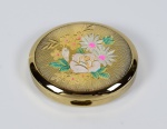 Caixa oval dourada para maquiagem. Tampa com decoração floral. Interior apresenta espelho, compartimento para maquiagem e caixa de música (necessitando reparo). Medidas: 8 cm x 7 cm x 2 cm (altura). Acompanha estojo.