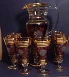 Jogo de jarra antiga vermelha com frisos dourados com seis taças longas medindo 31x18 e 16x6 cm.
