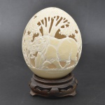 Escultura de ovo de avestruz finamente vazado e decorado com figuras de hipopotamo na Selva. Assinado Callisto, acompanha base em madeira (17cm.)