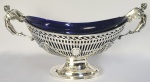 PRATA DE LEI INGLESA -  PORTENTOSO CENTRO DE MESA DE APARATO EM PRATA DE LEI COM MARCAS PARA CIDADE DE LONDRES. LETRA DATA 1903 E PRATEIRO E & CO. INTERIOR COM CRISTAL NA TONALIDADE AZUL COBALTO.  AS DUAS EXTREMIDADE  SÃO GUARNECIDAS POR LINDAS NINFAS ALADAS. O BOJO FENESTRADO É DECORADO COM LAURÉU FORMANDO GUIRLANDA. INGLATERRA, 1903. 42 CM DE COMPRIMENTO.  2330 G (PESO TOTAL)NOTA: Ninfas eram figuras mitológicas na Grécia Antiga, ligadas a elementos naturais. Em suma, os gregos acreditavam que as ninfas viviam em lagos, montanhas, campos e bosques. Além de serem responsáveis por levar felicidade e alegria para as pessoas, eram uma espécie de deusas-espírito da natureza que representavam o dom de fertilidade da natureza. Por fim, os gregos antigos eram muito devotos às ninfas, por isso, costumavam prestar homenagens a elas. A palavra ninfa (Nimphe) possui significados variados, como noiva, moça, mulher jovem ou botão de rosa e eram consideradas como a personificação de características de deuses e deusas gregas. Inclusive, algumas dessas figuras mitológicas eram aladas, como a Hérmia, por exemplo, considerada a deusa rainha de todas as ninfas. Além disso, as ninfas serviram de fonte de inspiração para a arte greco-romana. Por fim, as ninfas eram seres da natureza espiritual na mitologia grega, cuja personificação era a de mulheres jovens e atraentes.