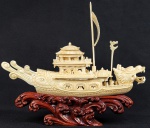 LINDA ESCULTURA EM MARFIM APRESENTANDO BARCO ESCULPIDO EM DETALHES COM PERSONAGENS DIVERSOS E PROA DECORADA COM FIGURA DE CABEÇA DE DRAGÃO. ASSENTE SOBRE BASE EM MADEIRA ENTALHADA SIMULANDO ONDAS. CHINA, INICIO DO SEC. XX. 31 CM DE COMPRIMENTO.