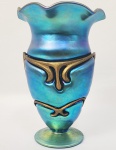 TIFFANY  (EX COLEÇÃO LUCIANO TADINI) ESPLENDOROSO VASO EM VIDRO FAVRILE IRIDESCENTE AZUL (TEL-EL-AMARNA OU AZUL TURQUESA) COM GUARNIÇÃO EM BRONZE. ASSINADO LOUIS CONFORT TIFFANY FAVRILE. O BRONZE ENVOLVE O VIDRO MOLDANDO-O AO SEU FEITIO. BORDA RECORTADA. BASE CIRCULAR. UMA PEÇA FANTÁSTICA, EM ÓTIMAS CONDIÇÕES, ASSINADO SOB A BASE. EUA, CIRCA DE 1903, 18,5 CM DE ALTURA. NOTA: O vidro Favrile é um tipo de vidro artístico iridescente desenvolvido por Louis Comfort Tiffany . Ele patenteou esse processo em 1894 e produziu o vidro para fabricação pela primeira vez em 1896, no Queens, Nova York. Ele difere da maioria dos vidros iridescentes porque a cor está enraizada no próprio vidro, além de possuir uma coloração distinta. Tiffany ganhou um grande prêmio na Exposição de Paris de 1900 por seu copo Favrile. Tiffany utilizou esse vidro nos vitrais desenhados e confeccionados por seu ateliê. Sua maior e mais significativa obra utilizando o vidro Favrile é Dream Garden (1916), encomendada pela Curtis Publishing Company para sua sede na Filadélfia e projetada por Maxfield Parrish . Agora é propriedade da Academia de Belas Artes da Pensilvânia .  Tiffany fundou sua primeira empresa de fabricação de vidro em 1892, 1 que ele chamou de Tiffany Glass and Decorating Company.  A fábrica, Tiffany Furnaces, estava localizada em Corona, Queens , Nova York.  Era administrado pelo imigrante inglês Arthur J. Nash , especialista em fabricação de vidro. Foi aqui que Tiffany desenvolveu seu método único de fabricação de vidro : tratar o vidro fundido com óxidos metálicos que foram absorvidos pelo vidro e criaram um luxuoso efeito de superfície iridescente. Tiffany trabalhou para desenvolver este novo vidro depois de ser fortemente influenciado por sua viagem à Europa em 1865. Em Londres visitou o South Kensington Museum, mais tarde rebatizado de Victoria and Albert Museum , cuja extensa coleção de vidros romanos e sírios o impressionou profundamente. Estes incluíam vidro iridescente. Ele também admirava a coloração do vidro medieval e acreditava que poderia melhorar a qualidade do vidro contemporâneo. Depois de muita experimentação e desenvolvimento, ele recebeu a patente do vidro Favrile em 1894.  Ele fez os primeiros objetos Favrile em 1896.  Na Exposição de Paris de 1900 , o vidro Favrile da Tiffany ganhou o grande prêmio da exposição.   Favrile é diferente de outros vidros iridescentes porque sua cor não está apenas na superfície, mas em parte do vidro.  O nome comercial original , Fabrile , foi derivado de uma palavra do inglês antigo , fabrile , que significa "feito à mão".  Tiffany mais tarde mudou a palavra para Favrile , "já que soava melhor". Algumas das cores distintivas do vidro Favrile incluem "Gold Lustre", "Samian Red", "Mazarin Blue", "Tel-el-amarna" (ou Azul Turquesa) e "Aquamarine".