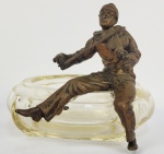 PIERROT VIOLINISTA  BELO DESPOJADOR EM CRISTAL DE BELO FEITIO ORNAMENTADO COM FIGURA DE PIERROT EM BRONZE TOCANDO VIOLINO. EUROPA, INICIO DO SEC. XX. 18 CM DE DIAMETRONOTA: O Pierrot é um personagem da commedia dell'arte, uma variação francesa do Pedrolino italiano.1 O seu caráter é aquele de um palhaço triste, apaixonado pela Colombina, que inevitavelmente lhe parte o coração e o deixa pelo Arlequim, mas depois Colombina descobre o amor de Pierrot por ela, despede-se de Arlequim e reencontra Pierrot com quem passa a viver junto em um relacionamento com muita felicidade. É normalmente representado a usar roupas largas e brancas, por vezes metade pretas, rosto branco e uma lágrima desenhada abaixo dos olhos. A característica principal do seu comportamento é a sua ingenuidade, e é visto como um bobo, sendo sempre o alvo de partidas, mas mesmo assim continua a confiar nas pessoas. Pierrot também é apresentado como sendo lunático, distante e inconsciente da realidade. A versão francesa da personagem foi feita por Jean-Gaspard Deburau (1796-1846). Ele é o protagonista da famosa canção folclórica francesa "Au Clair de la Lune". Soletrado "Pierrot", a personagem é uma atração importante em Bakken, o parque de atrações mais velho do mundo, na Dinamarca. Segundo a publicidade de Bakken, a personagem tem mais de quatro mil anos, e veio da Turquia (conhecida como Ásia Menor). Também é dito que nos tempos antigos, a boca larga vermelha era feita através do corte físico da boca para alargá-la. O cantor de cabaré russo do século XX, Alexander Vertinsky, era famoso pela sua atuação como Pierrot, em que usava uma roupa preta e punha pó branco no rosto .