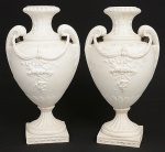 Par de vasos franceses de meados do século XIX, c1860, executados em porcelana de biscuit na tonalidade branca, estilo Luís XVI. Bojo oval dotado de decoração relevada modelada na própria pasta, guirlandas de flores suspensas pelas duas alças laterais em forma de folhagem encaracolada, fuste e gargalo com sulcos verticais, assente sobre base quadrangular. Estrutura espessa e pesada. Med.: Alt. 32,5 x Comp. 18 x Larg. 16 cm.  Apresenta cola de massa marrom no fundo fixando os parafusos das peças no fundo da base.