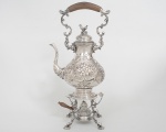 Samovar Russo em metal espessurado a prata finamente cinzelado e guilhochado decorado em relevo com flore e ramagens, pega da tampa no formato de galinaço apoiada sobre trempe com quatro pés recurvos com pegas do queimador e alça em madeira nobre isolante. Completo. Medida: 46 cm de altura.
