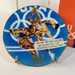 ESPORTE - OLIMPÍADAS. Prato em porcelana comemorativo / alusivo aos JOGOS OLIMPICOS DE ATLANTA 1996 - Team U.S.A., produto licenciado pela AVON PRODUCTS, INC NEW YORK, com acabamento em ouro 22 K, acondicionado em estojo original, souvenir decorativo medindo 12,8 centímetros de diâmetro, sem uso.