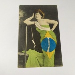 ANTIGO CARTÃO POSTAL colorizado, representado por uma linda mulher vestindo a Bandeira do Brasil. Na faixa branca da bandeira está escrito SAUDADES ao invés de Ordem e Progresso. Não determinamos a época do postal.
