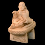 Netsuke esculpido em marfim, representando musicista tocando flauta, ajoelhada sobre banco. Assinado. 4.5 x 2 x 3.5 cm.
