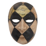 Máscara de fantasia, possivelmente do Carnaval de Veneza, ornada em xadrez preto e creme, realçada no topo por partituras musicais. 18 x 10 cm.