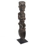 Estatueta africana em madeira esculpida, representando mulher agachada sobre base no formato de cabeça com rosto escavado. África Ocidental. Base quadrangular. Peça pertencente ao acervo da Família de Paulo Fachini.