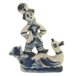 Grupo escultórico em porcelana policromada representando menino encimado e pato estilizado. Marca da manufatura no fundo da peça. 13 x 10 cm.