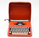 Antiga máquina de escrever no tom laranja da marca "Hermes Baby". Med.: 29 X 27 X 7 cm.