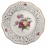 BAVÁRIA - Prato confeccionado em porcelana alemã esmaltada na tonalidade branca e com flores ao centro, bordas em vazamento. Possui registro da manufatura. Mede 19cm de diâmetro.