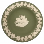 WEDGWOOD - Inglaterra. Pequeno prato confeccionado em biscuit na tonalidade verde, decorado por uvas e folhas de parreira e cena de cavalaria no centro em relevo e na tonalidade branca. Possui registro da manufatura. Mede 11cm de diâmetro.