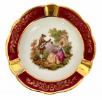 LIMOGES FRANÇA - Antigo cinzeiro em pasta de porcelana francesa Limoges, adornado ao centro com cena galante em rica policromia e contorno em volutas dourados sobre fundo marsala. Mede 12cm de diâmetro.